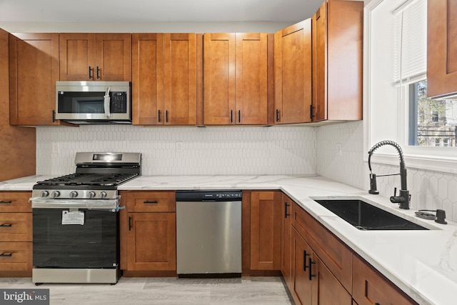 kitchen with a sink, stainless steel appliances, backsplash, light wood-style flooring, and light stone counters