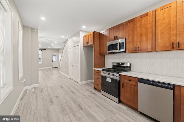 kitchen with brown cabinetry, tasteful backsplash, appliances with stainless steel finishes, light stone counters, and light wood finished floors