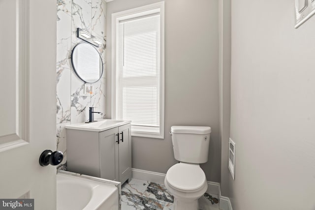 bathroom with baseboards, a bathing tub, toilet, vanity, and marble finish floor