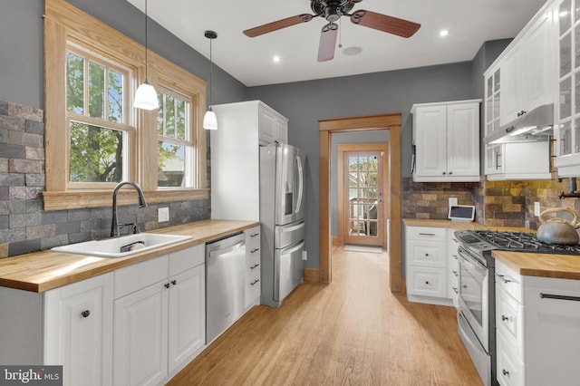 kitchen with butcher block countertops, decorative backsplash, light wood-style floors, appliances with stainless steel finishes, and a sink