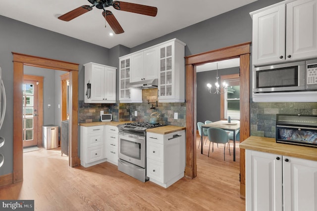 kitchen with butcher block countertops, stainless steel appliances, light wood-type flooring, and ceiling fan with notable chandelier
