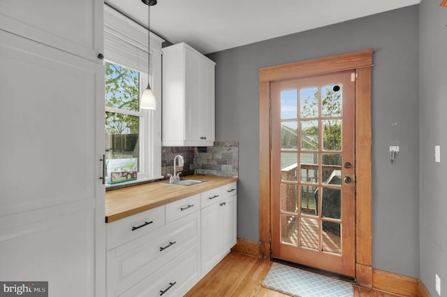 interior space with a sink, light wood-style floors, tasteful backsplash, baseboards, and pendant lighting