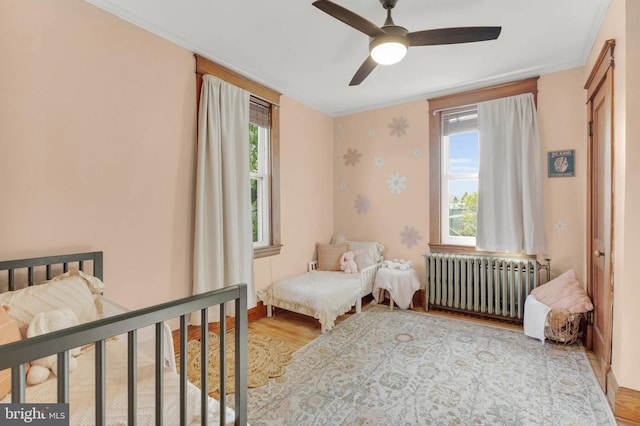 bedroom with wood finished floors, radiator heating unit, ceiling fan, baseboards, and crown molding