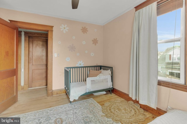 bedroom featuring a ceiling fan, baseboards, ornamental molding, wallpapered walls, and wood finished floors
