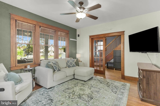 living room with a ceiling fan, baseboards, stairs, and light wood-type flooring