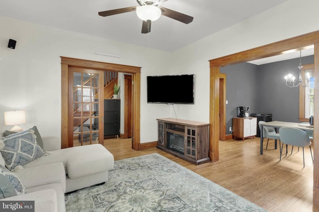 living room featuring baseboards, wood finished floors, and ceiling fan with notable chandelier