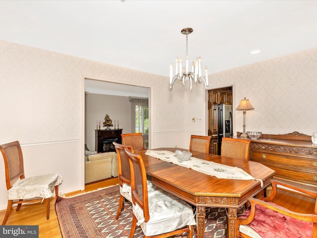 dining space with baseboards, light wood finished floors, wallpapered walls, and a notable chandelier