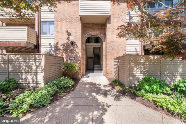 view of exterior entry featuring brick siding and fence