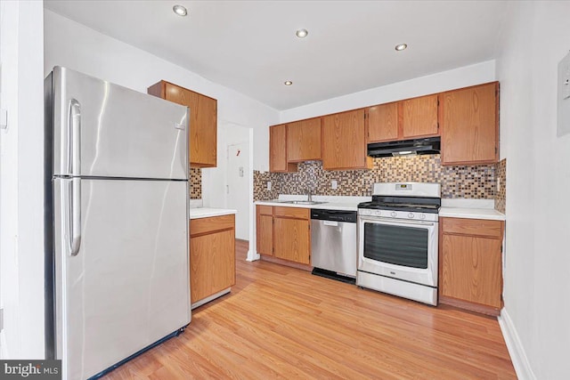 kitchen featuring appliances with stainless steel finishes, tasteful backsplash, under cabinet range hood, and light wood-style flooring