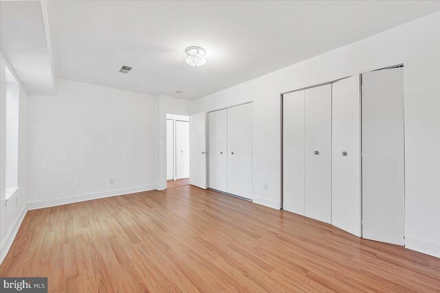 unfurnished bedroom with visible vents, baseboards, multiple closets, and light wood finished floors