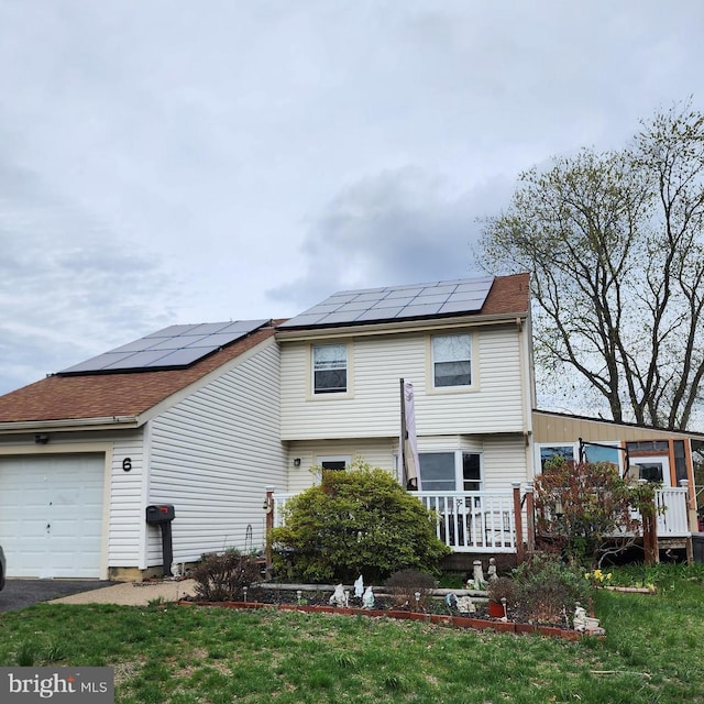 back of house with an attached garage, roof mounted solar panels, and a lawn