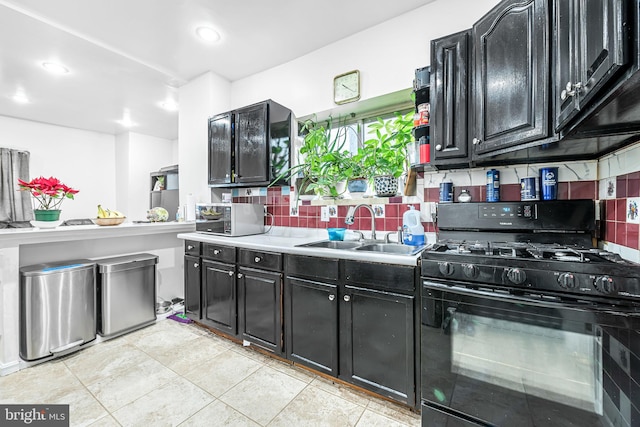 kitchen with a sink, backsplash, dark cabinetry, and black gas stove