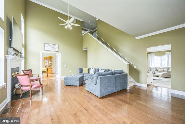 living room with baseboards, wood finished floors, ceiling fan, stairway, and ornamental molding