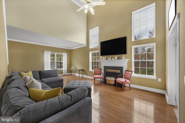 living room with a high ceiling, wood finished floors, a ceiling fan, baseboards, and a fireplace