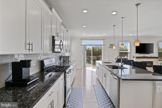 kitchen featuring white cabinets, a center island with sink, decorative backsplash, stainless steel appliances, and a sink