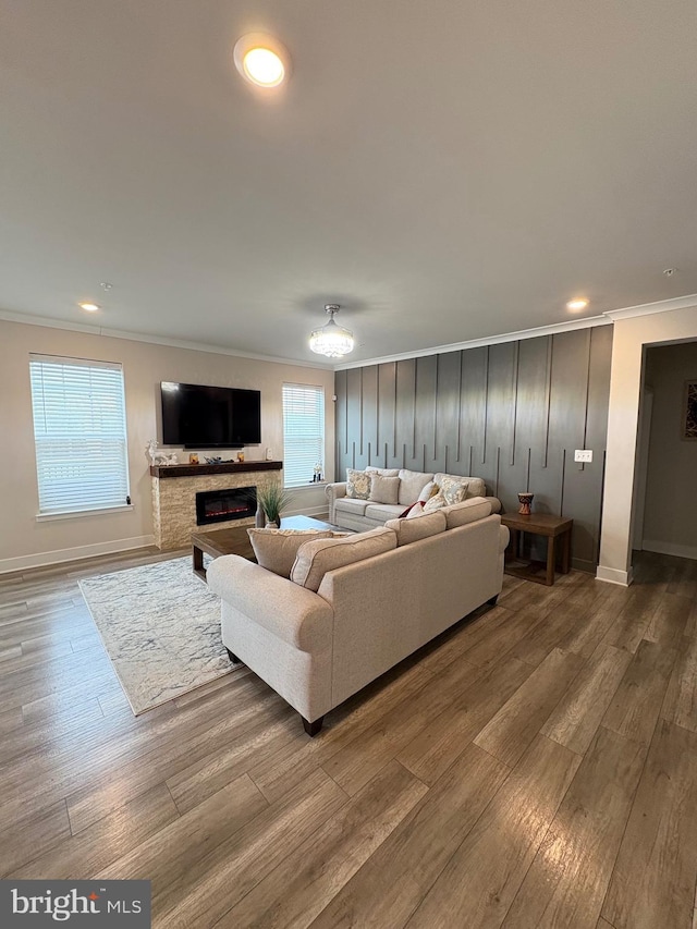 living area with a glass covered fireplace, baseboards, ornamental molding, recessed lighting, and wood finished floors