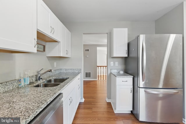 kitchen with appliances with stainless steel finishes, a sink, light wood finished floors, and white cabinetry