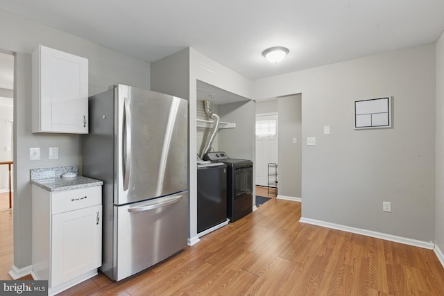 kitchen featuring freestanding refrigerator, washing machine and clothes dryer, light wood-type flooring, white cabinetry, and baseboards