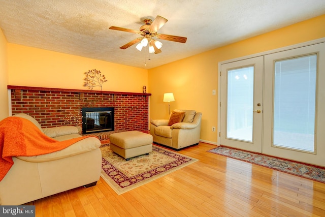 living room with a textured ceiling, wood finished floors, a brick fireplace, and ceiling fan