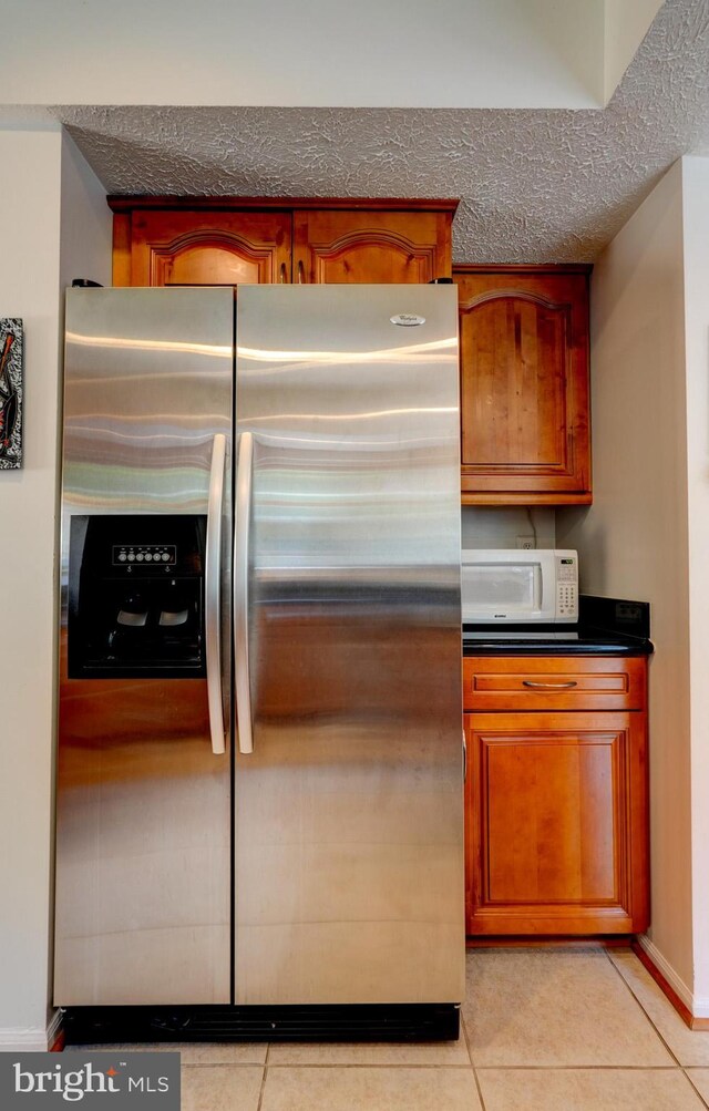 kitchen featuring brown cabinets, dark countertops, light tile patterned floors, white microwave, and stainless steel fridge