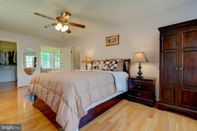 bedroom with light wood-type flooring, baseboards, a ceiling fan, a closet, and a walk in closet