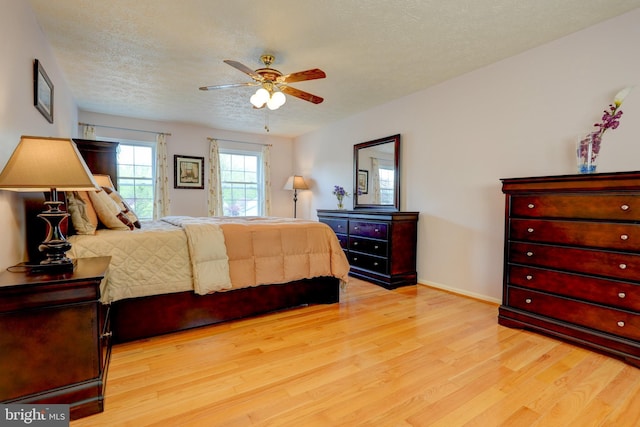 bedroom with baseboards, a ceiling fan, a textured ceiling, and light wood-type flooring