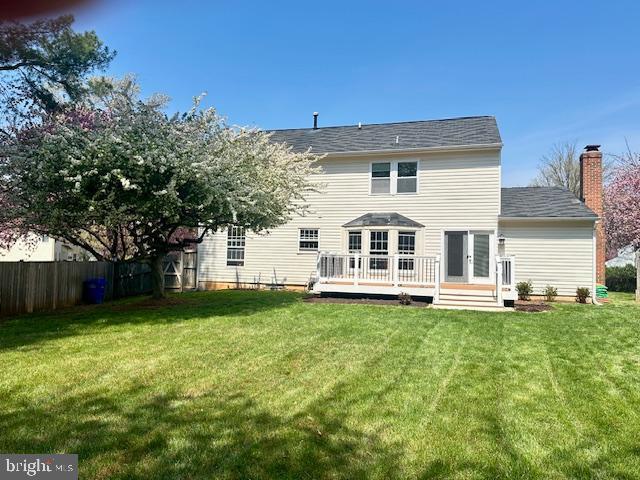 back of house featuring fence, a wooden deck, a chimney, and a yard