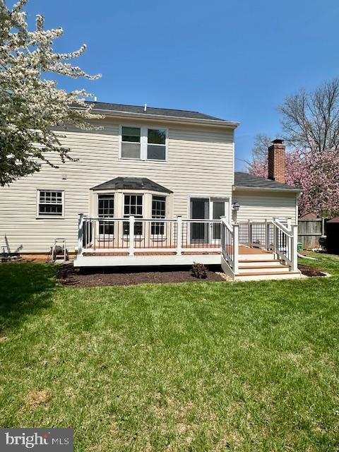 back of house featuring a wooden deck, a chimney, and a yard