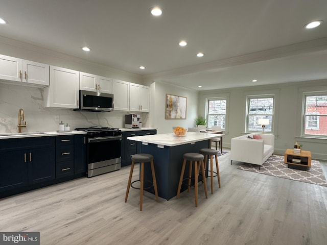 kitchen featuring a center island, crown molding, appliances with stainless steel finishes, light wood finished floors, and a sink