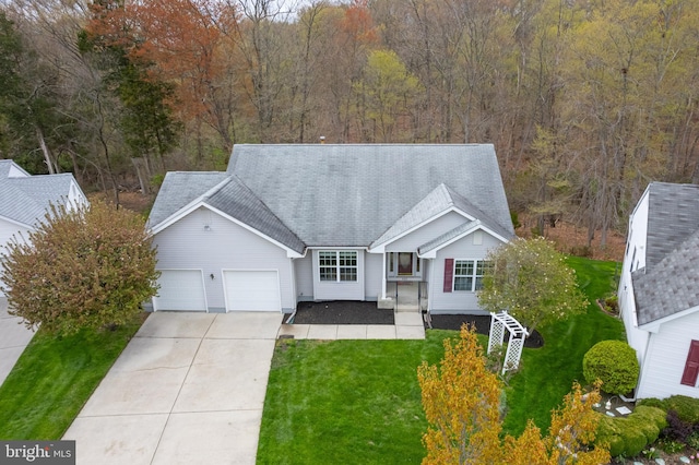 single story home featuring concrete driveway, a garage, a forest view, and a front yard
