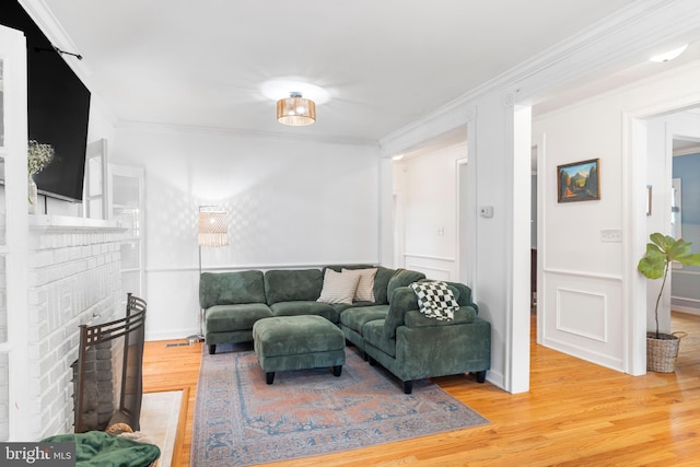 living room featuring a fireplace, ornamental molding, a decorative wall, and wood finished floors