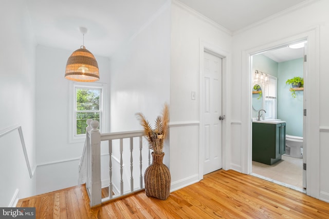 hallway with a sink, ornamental molding, an upstairs landing, and wood finished floors