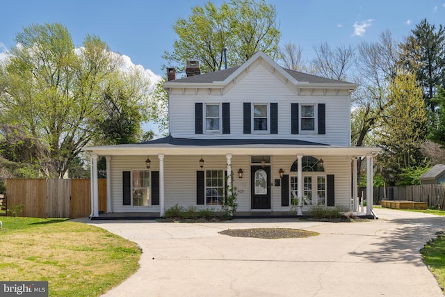 view of front of house with a porch, a chimney, and fence