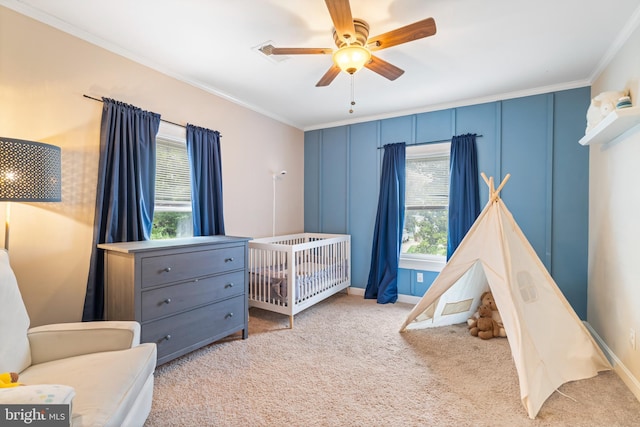 carpeted bedroom with crown molding, baseboards, a ceiling fan, and a nursery area