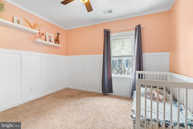 carpeted bedroom featuring crown molding, a decorative wall, wainscoting, and visible vents