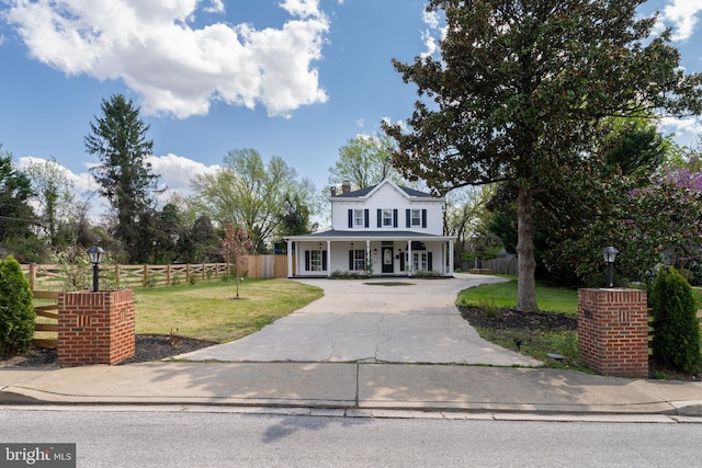 traditional-style home featuring a front yard, a porch, fence, and concrete driveway