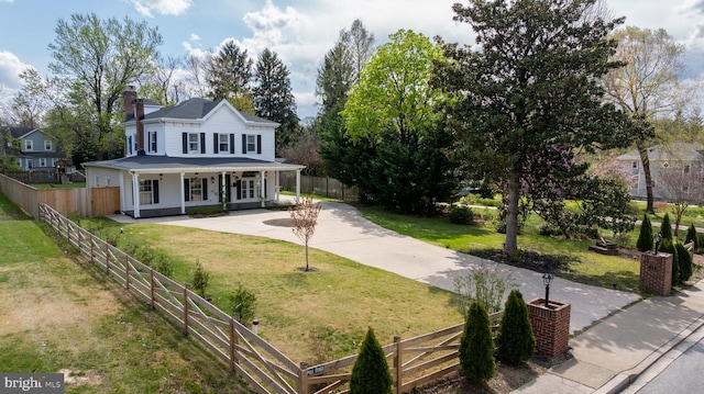 view of front of property with a porch, fence private yard, a chimney, a front lawn, and driveway