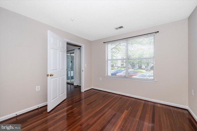 unfurnished bedroom with dark wood-style floors, baseboards, and visible vents