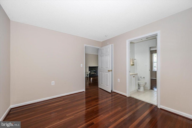 unfurnished bedroom featuring wood finished floors, connected bathroom, and baseboards