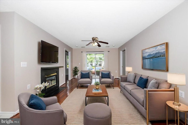 living area featuring baseboards, wood finished floors, a ceiling fan, and a glass covered fireplace
