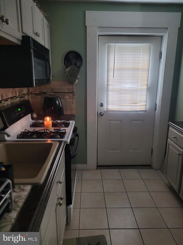 2027 Anchor St, Philadelphia, PA 19124 - kitchen with light tile patterned floors, black microwave, white cabinets, range with gas stovetop, and decorative backsplash