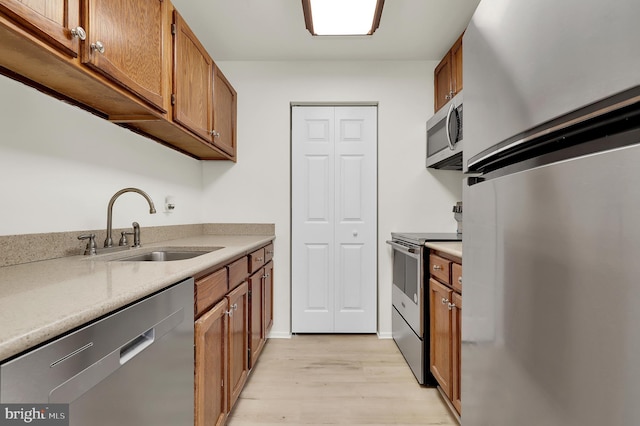 kitchen featuring brown cabinets, a sink, stainless steel appliances, light wood-style flooring, and light countertops