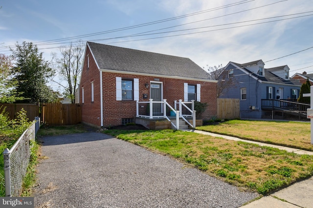 view of front of property with brick siding, a front yard, fence, and a shingled roof