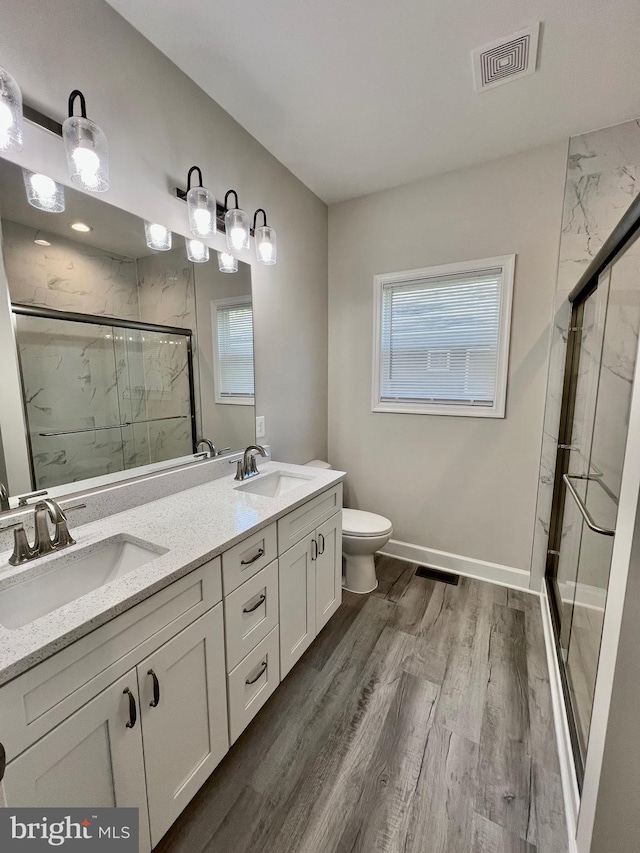 bathroom with a sink, visible vents, a marble finish shower, and wood finished floors
