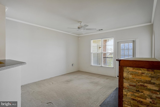 carpeted spare room with visible vents, crown molding, baseboards, and ceiling fan
