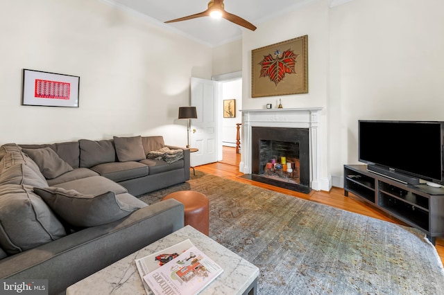 living area with crown molding, a fireplace with flush hearth, a ceiling fan, and wood finished floors