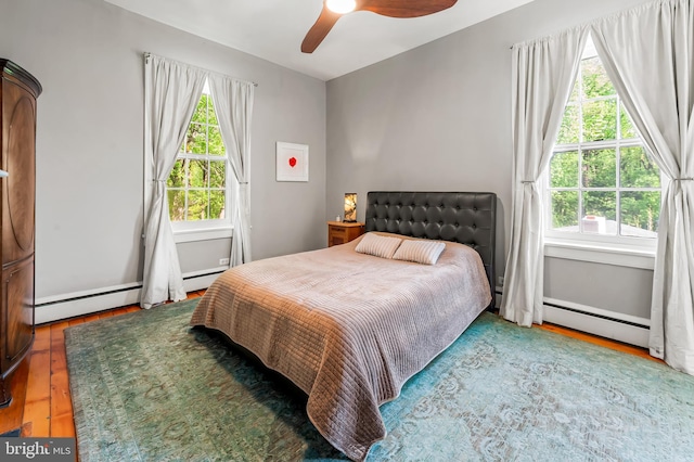 bedroom with multiple windows, a ceiling fan, a baseboard heating unit, and wood finished floors