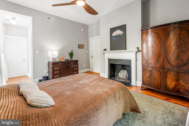bedroom featuring ceiling fan, visible vents, a fireplace, wood finished floors, and baseboards
