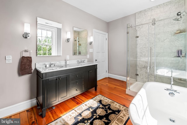 full bathroom with double vanity, wood finished floors, baseboards, a soaking tub, and a stall shower