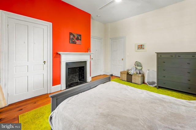 bedroom with a fireplace with raised hearth, ceiling fan, and wood finished floors
